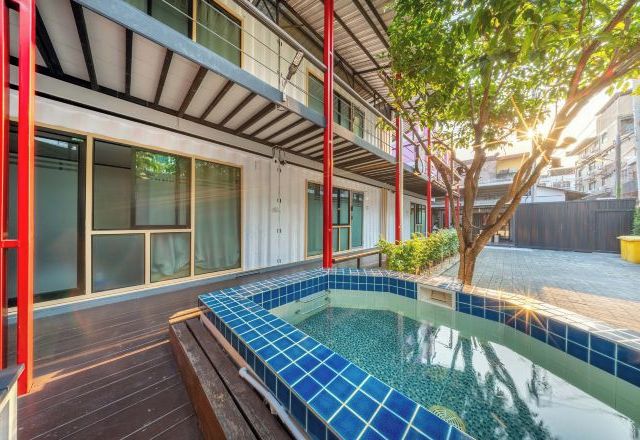 A modern building with a rooftop pool area, large windows, and a tree.