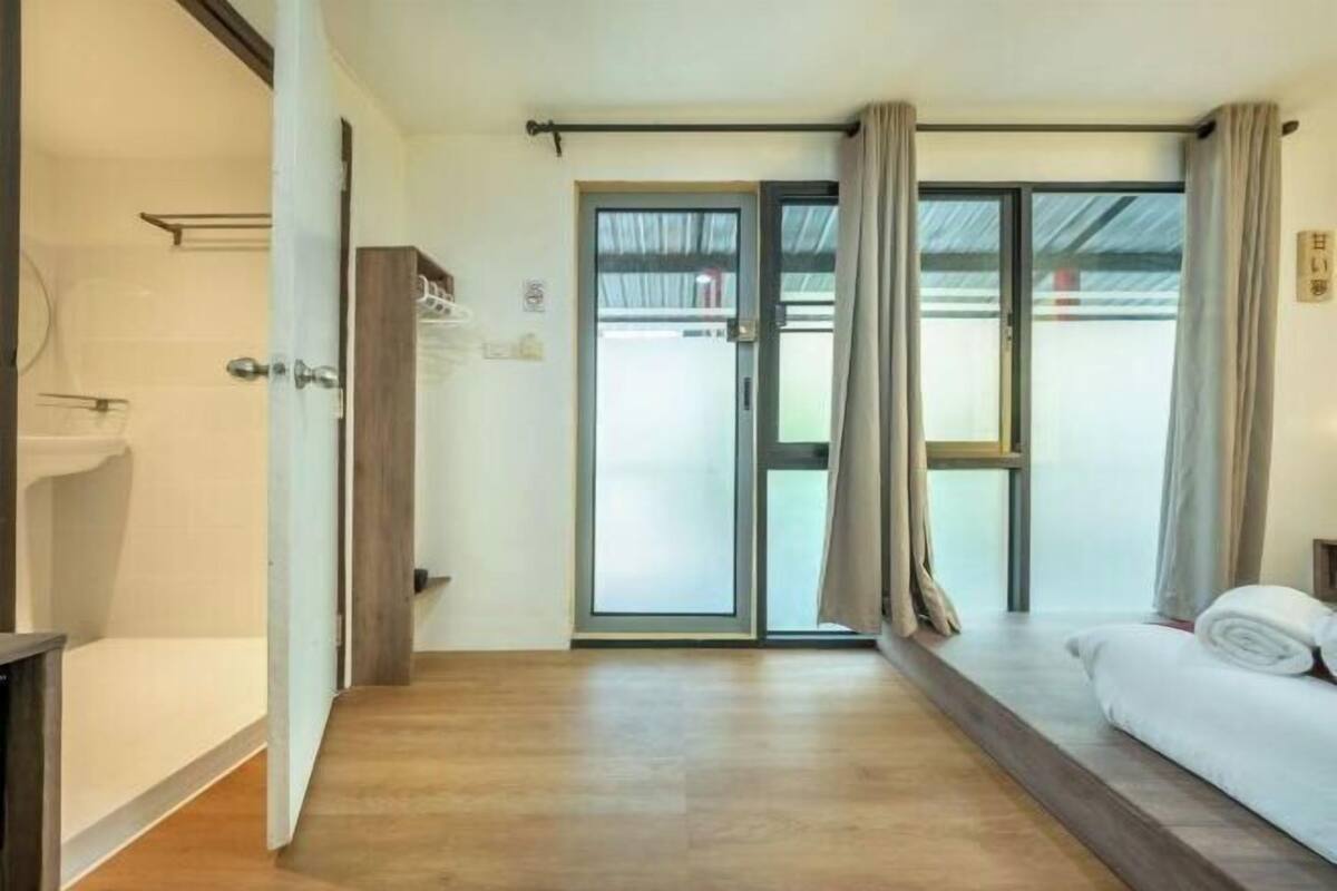 Ein Hotelzimmer mit Holzboden, einem Bett mit weißer Bettwäsche, einer Schiebeglastür und einem Duschbereich.