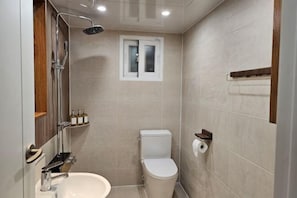 Un baño con inodoro, lavabo, ducha y una ventana pequeña.