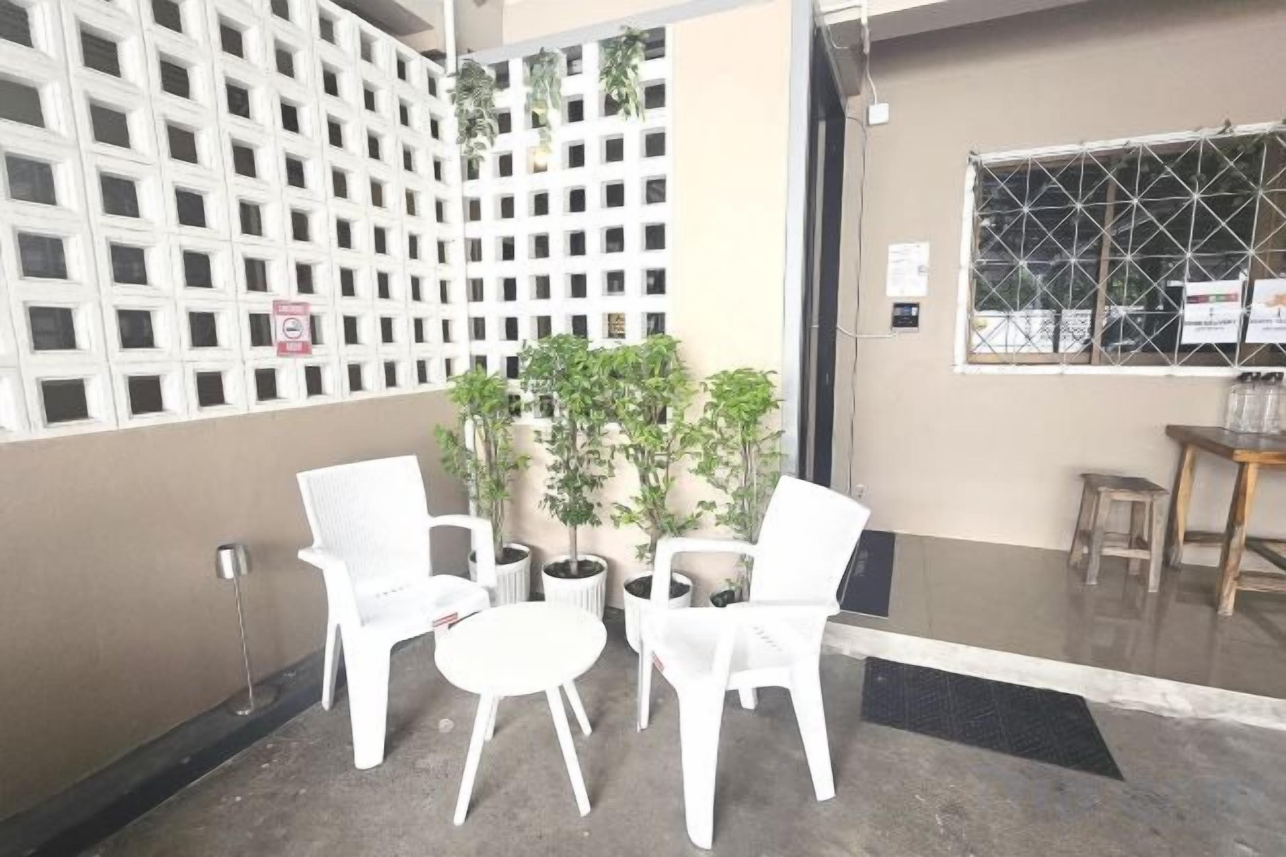 A seating area with white chairs and a small table, a potted plant, and a window with a metal grid.