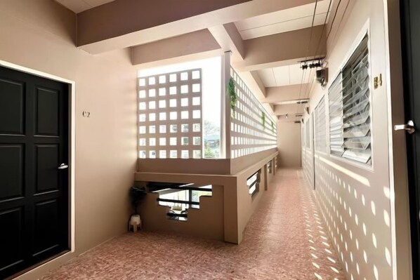 Un couloir avec une porte noire, un mur blanc orné d’un motif quadrillé et une fenêtre avec des stores.