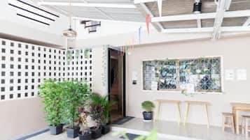 An indoor space with a ceiling with exposed beams, a white wall with a grid pattern, a window with a view, and several potted plants.