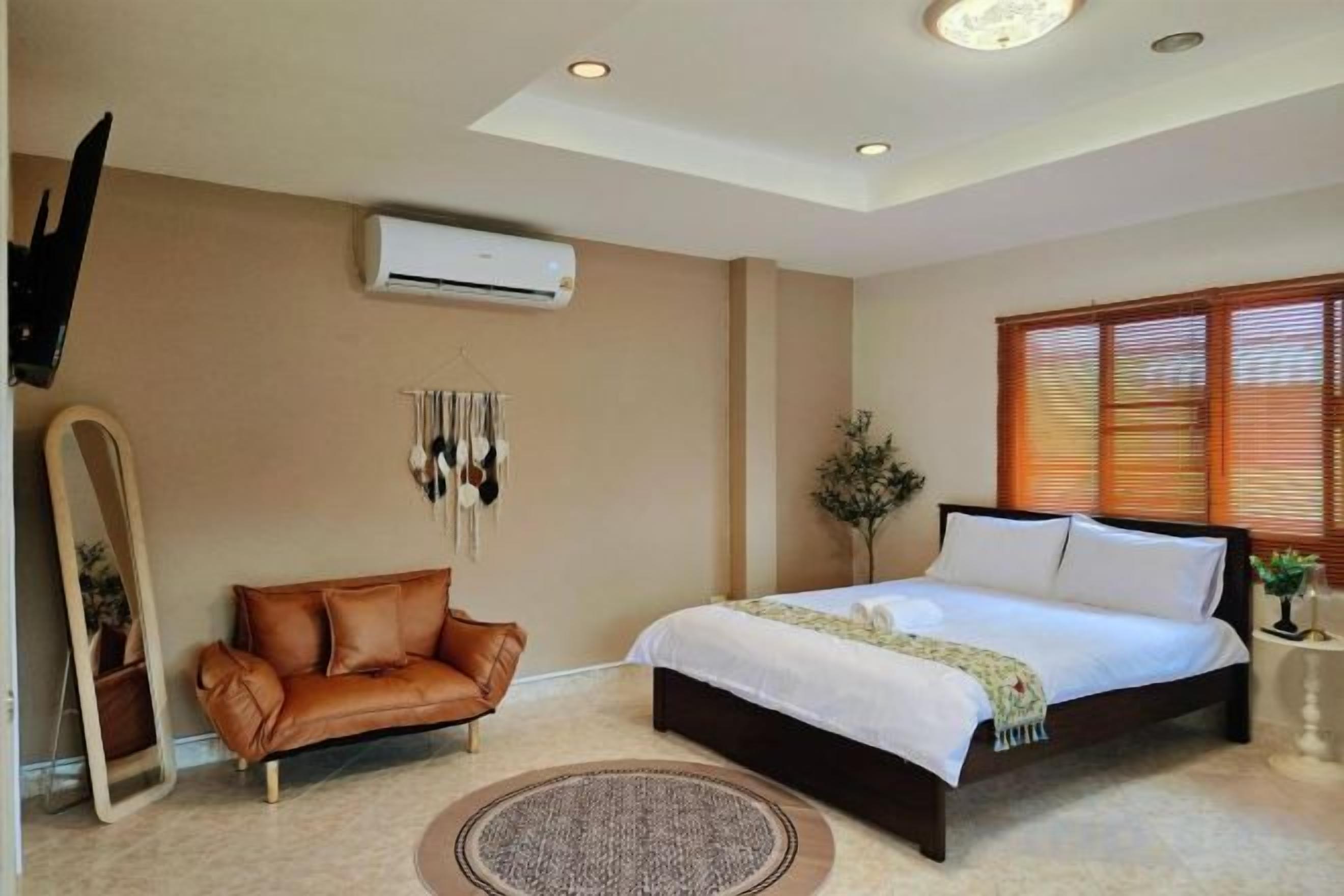 A bedroom with a bed, a leather sofa, a mirror, and a window with blinds.