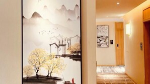 A hallway with a traditional painting of mountains, trees, and a traditional building. There is a wooden door and a framed artwork on the wall. - Youngsun Hotel (Sihanoukville)