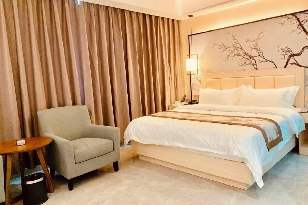 A hotel room with a bed, a chair, a nightstand, and a lamp.