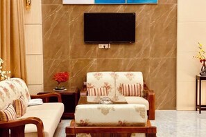 A living room with a sofa, ottoman, and a flat-screen TV mounted on the wall. - Youngsun Hotel (Sihanoukville)