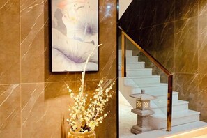 A marble wall with a framed artwork, a staircase with a wooden handrail, and a decorative vase with branches. - Youngsun Hotel (Sihanoukville)