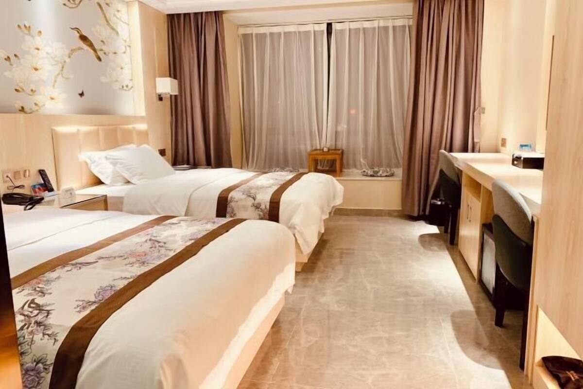 A hotel room with two beds, a desk, and a window with curtains.