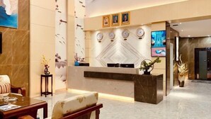 A hotel reception area with a marble reception desk, wall-mounted clocks, and framed portraits above the desk. - Youngsun Hotel (Sihanoukville)
