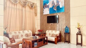 A living room with a sofa set, a coffee table, a TV mounted on the wall, and a large abstract painting. - Youngsun Hotel (Sihanoukville)