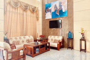 A living room with a sofa set, a coffee table, a flat-screen TV mounted on the wall, and a large painting. - Youngsun Hotel (Sihanoukville)
