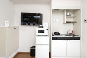 Une cuisine compacte équipée d’un four à micro-ondes, d’un petit réfrigérateur, d’un évier et d’une poubelle noire.