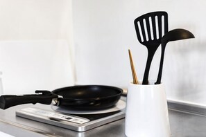 Un plan de travail de cuisine avec une poêle, des spatules et un récipient blanc.