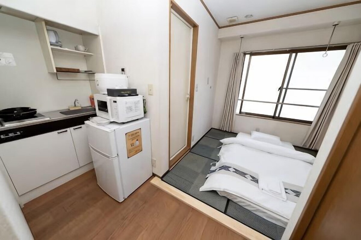 Une pièce compacte comprenant un coin cuisine, un lit, une fenêtre et un petit espace de rangement.