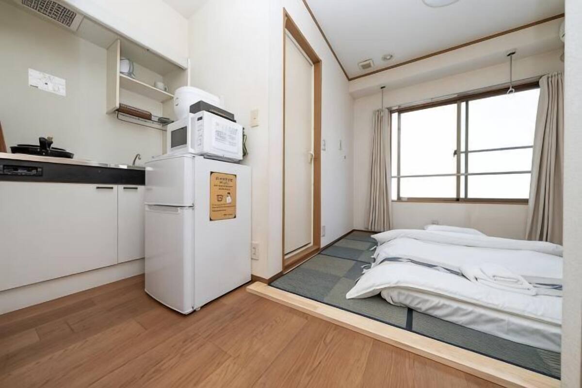 Quarto compacto com cozinha compacta, cama e janela.