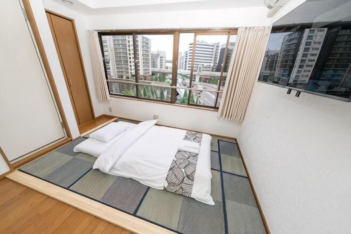 Une chambre avec un lit, une fenêtre donnant sur des immeubles et une porte coulissante.