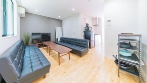 A modern living room with a sofa, a coffee table, a TV, and a kitchen area with a fridge and a shelf. - 10min on foot from Hirai Station. 11min by train to Akihabara Station. (Tokyo)