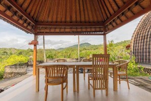 Ein überdachter Außenbereich mit Tisch und Stühlen mit Blick auf eine hügelige Landschaft.