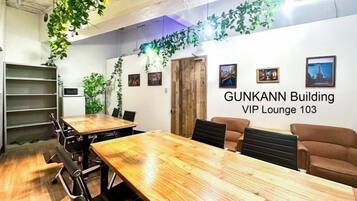 Een vergaderruimte met een lange houten tafel, stoelen en een whiteboard. Er staan planten op de muren en een deur met de tekst 'GUNKANN Building VIP Lounge 103'.
