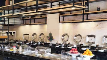 Uma área de buffet com diversas estações de serviço, cubas de vidro transparentes e uma variedade de alimentos.