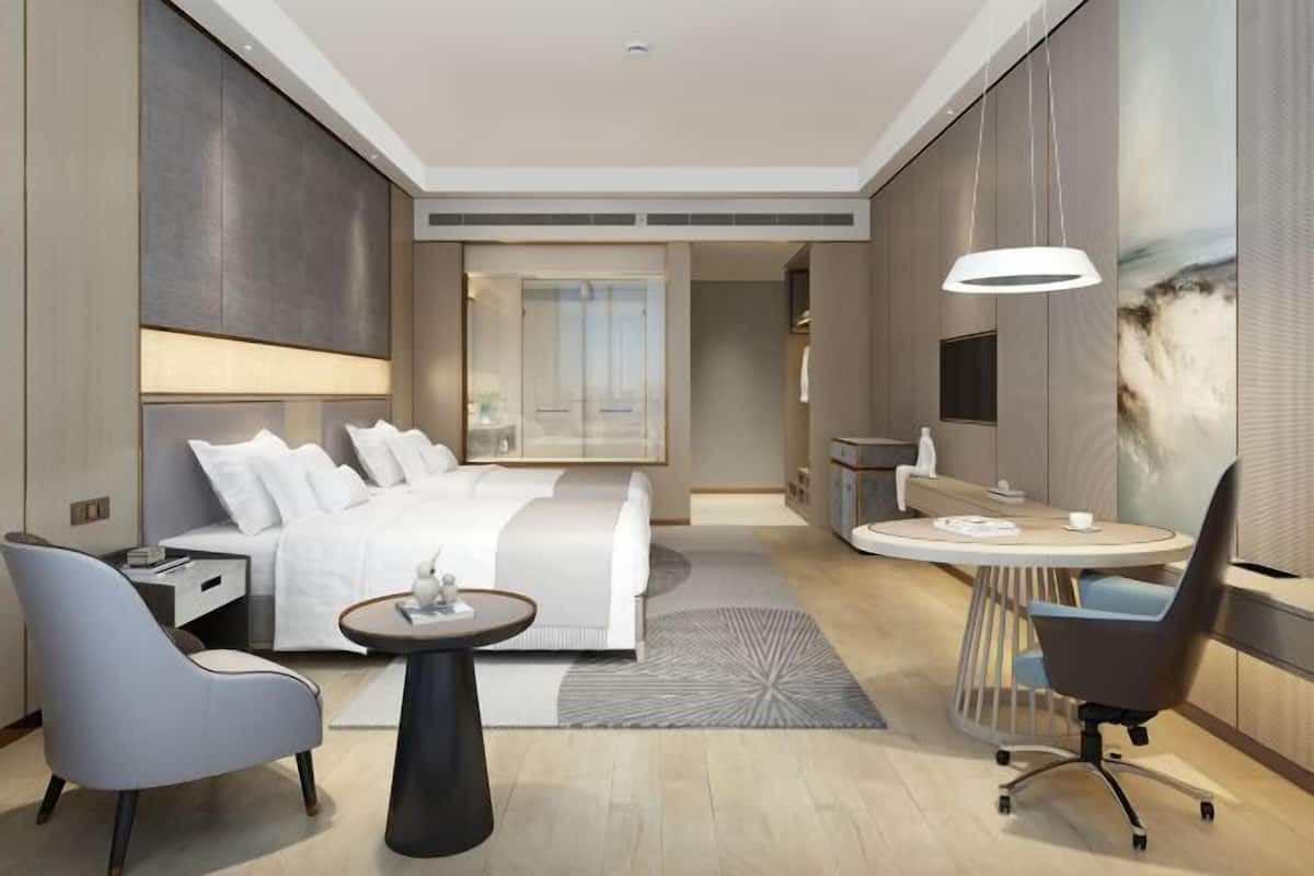 Une chambre d’hôtel moderne équipée d’un lit, d’un bureau, d’une chaise, d’une table ronde et d’un téléviseur.