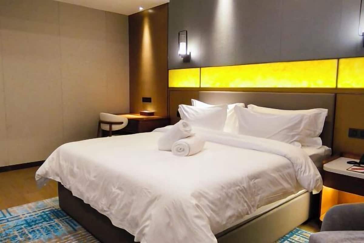 Une chambre d’hôtel avec un grand lit, une table de chevet, une chaise et une lampe fixée au mur.