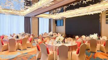 Un salón de banquetes con mesas redondas, sillas y centros de mesa florales.