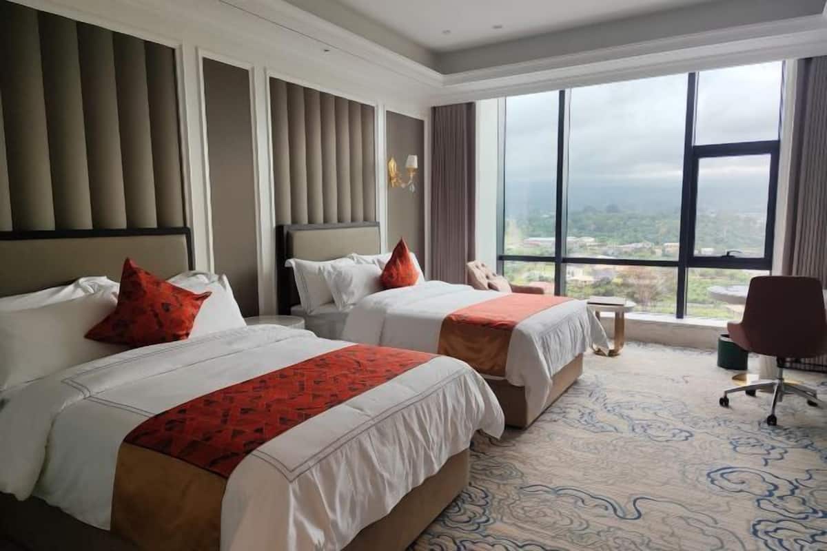 Une chambre d’hôtel avec deux lits, une grande fenêtre donnant sur la ville, une petite table et une chaise.