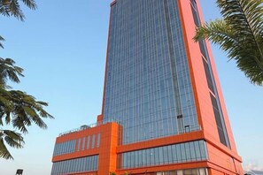 A tall, modern building with a glass facade and a red base. - Hotel Anda (Malabo)