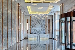 A modern hotel lobby with a marble reception desk, a geometric patterned wall, and a glass partition.