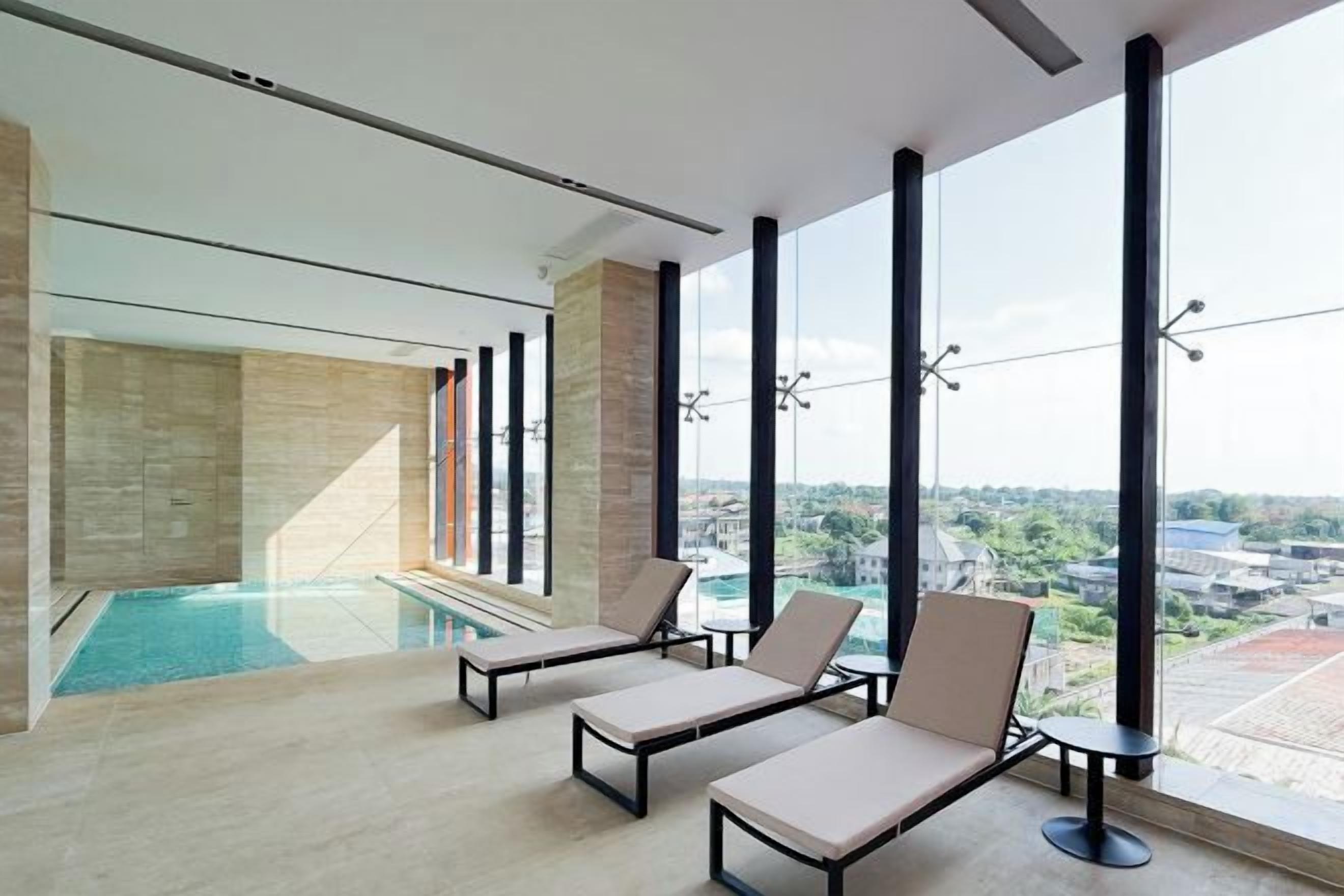 Un área de piscina interior moderna con sillones de descanso y grandes ventanales con vistas a la ciudad.