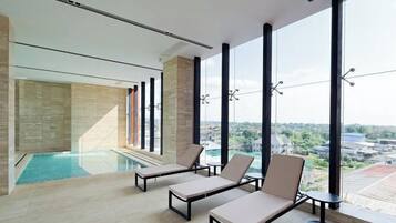 Un área de piscina interior moderna con sillones de descanso y grandes ventanales con vistas a la ciudad.