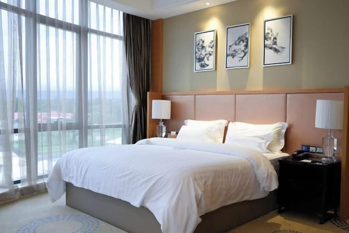 Une chambre d’hôtel avec un grand lit, une table de chevet, une fenêtre avec des rideaux et trois tableaux encadrés accrochés au mur.