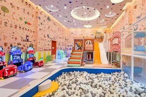 Lasten leikkialue, jossa on pallomeri, kiipeilytelineitä ja värikkäitä ajettavia leluja.