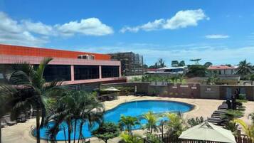 Piscina com design curvo, rodeada por palmeiras e um edifício com telhado vermelho.
