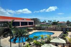 A swimming pool with a curved design, surrounded by palm trees and a building with a red roof. - Hotel Anda (Malabo)