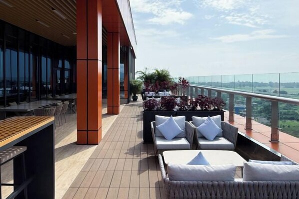 A rooftop terrace with outdoor seating, a view of the city, and a glass railing.