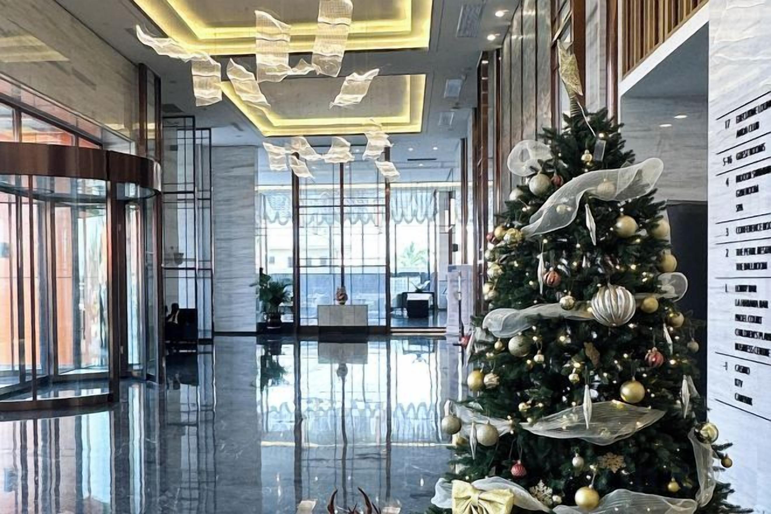 Un hall d’hôtel moderne, agrémenté d’un grand sapin de Noël, de revêtements de sol réfléchissants et d’un plafond haut orné de luminaires originaux.