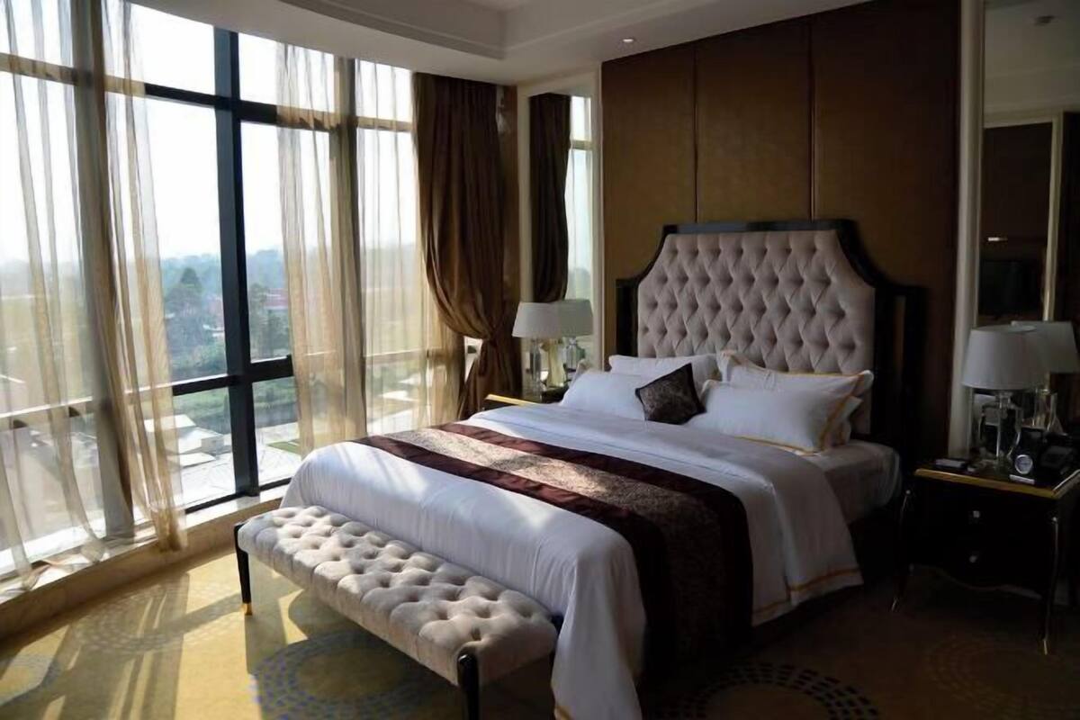 Une chambre d’hôtel avec un grand lit, une banquette, une table de chevet, une lampe et une vue sur l’extérieur.