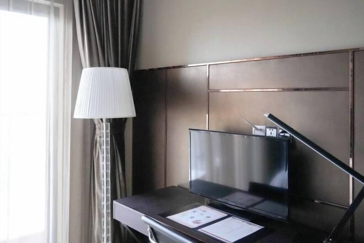 Une chambre d’hôtel équipée d’une télévision à écran plat, d’un bureau avec une lampe et d’une fenêtre avec des rideaux.