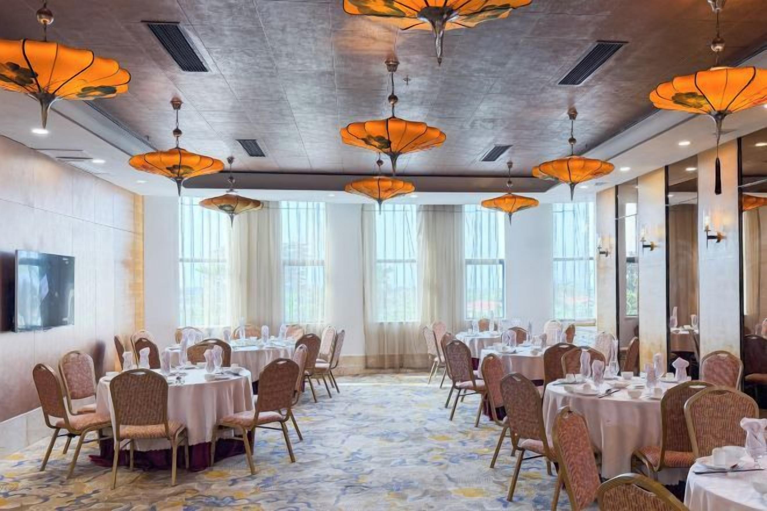 A banquet hall with round tables, chairs, and orange hanging lamps.