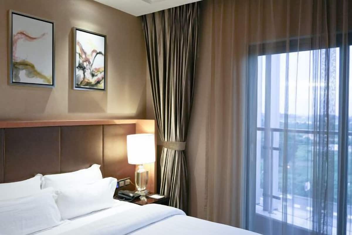 Une chambre d’hôtel avec un lit, une table de chevet avec une lampe, une fenêtre avec des rideaux et deux tableaux abstraits accrochés au mur.