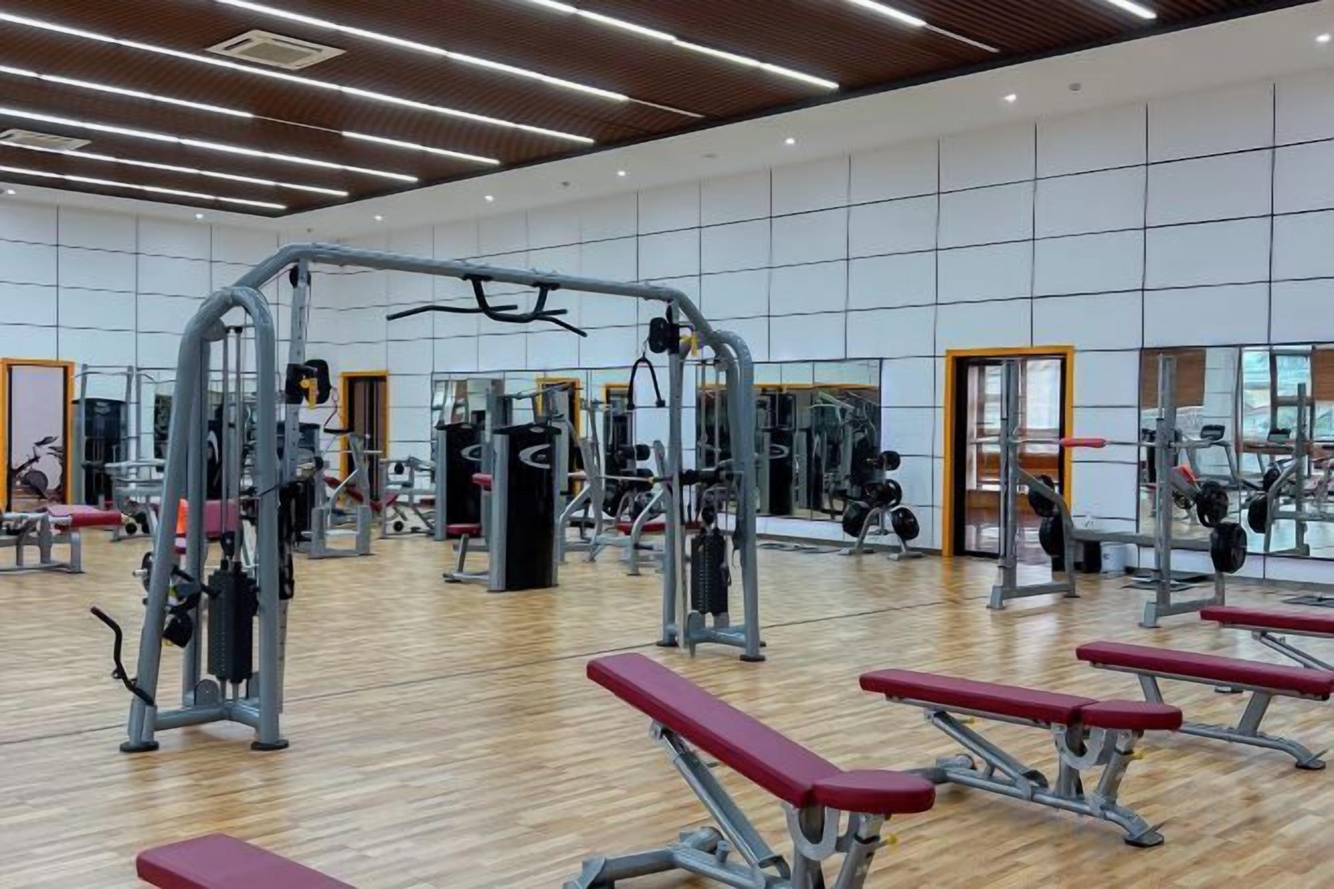 Academia com diversos equipamentos de exercício, piso de madeira e espelhos nas paredes.