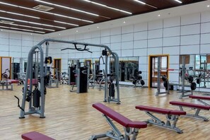A gym with various exercise equipment, wooden flooring, and mirrors on the walls.