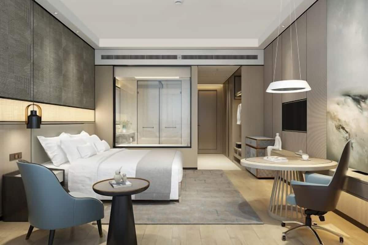 Une chambre d’hôtel moderne équipée d’un lit, d’un bureau, d’une chaise, d’une télévision et d’un grand miroir.