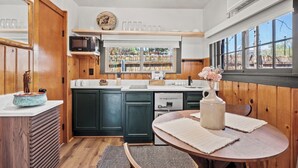 A compact kitchen with wooden cabinetry, a built-in microwave, and a dining area with a table and chairs. - Timber Lodge Cabin 02 (Colorado Springs)