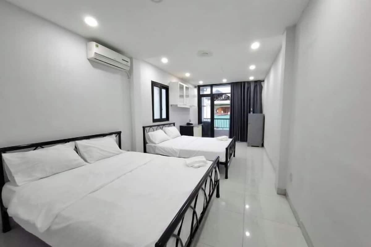 A hotel room with two beds, a window with curtains, an air conditioning unit, and a small kitchenette area.