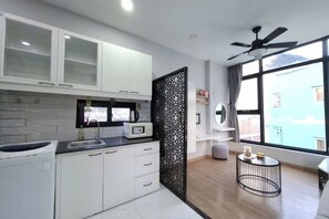 Une cuisine moderne avec des meubles blancs, un séparateur décoratif noir, un ventilateur de plafond et une grande fenêtre offrant une belle vue.