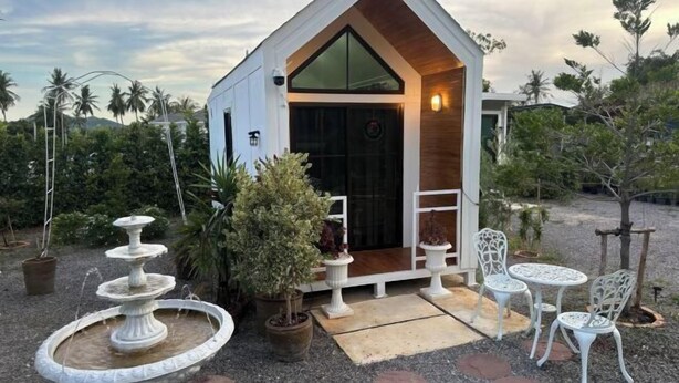 Un edifici petit, de planta baixa i color blanc, amb teulada triangular, una porta d'entrada i una petita zona de porxo. Hi ha mobiliari per a l'exterior i una font.