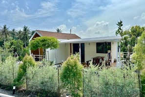 A single-story house with a white exterior and a brown roof, surrounded by a fence and greenery. - The Aura Pranburi (Pran Buri)